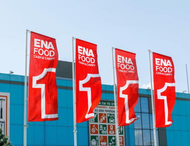 Four red flags with the logo from the supermarket ENA waving in front of a building